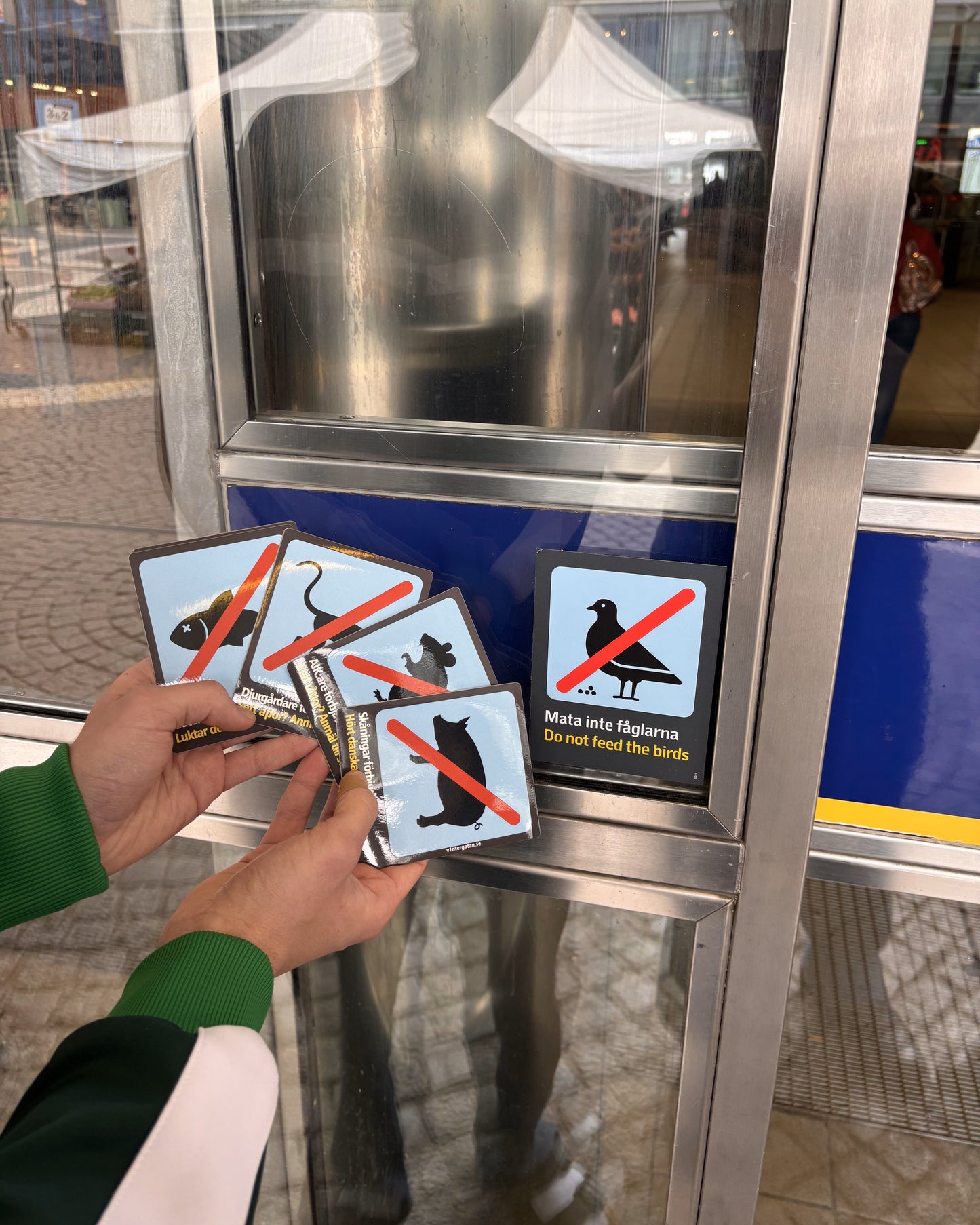 Vintergatans SL-pack med Bajen-tema. Hand håller Djurgårdare, AIK-are och Göteborgare klistermärken vid tunnelbanans förbudsskylt.